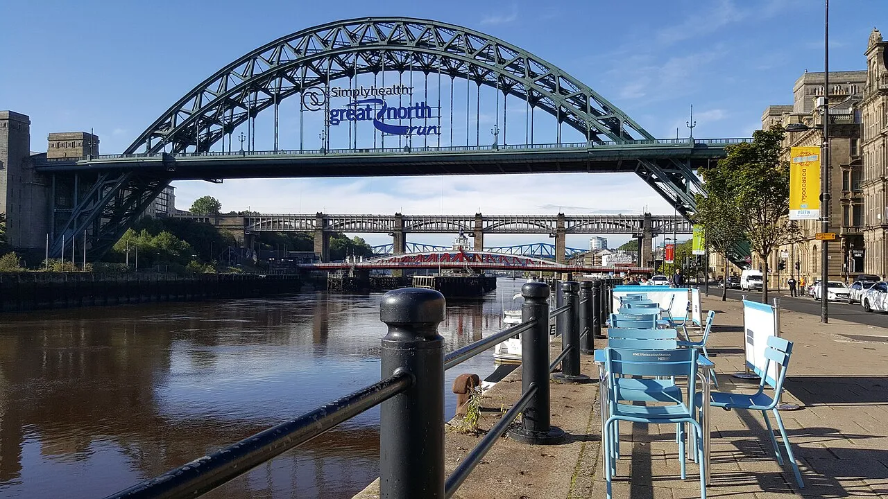 The Tyne Bridge arching over the river, seen from the Newcastle Quayside with café tables by the railings