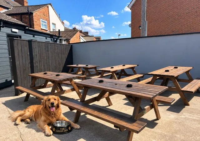 A golden retriever lying by a Green Inn water bowl among the picnic benches in the Green Inn beer garden